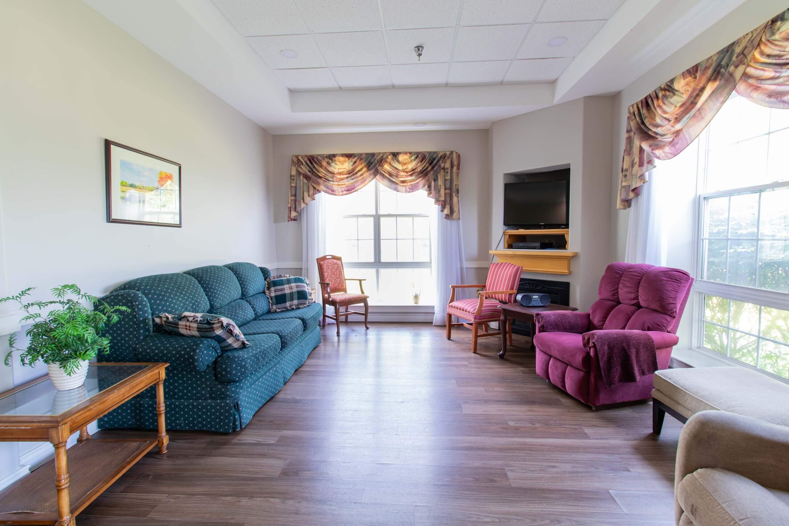 Resident seating Area by a window with a blue couch and 3 red chairs.