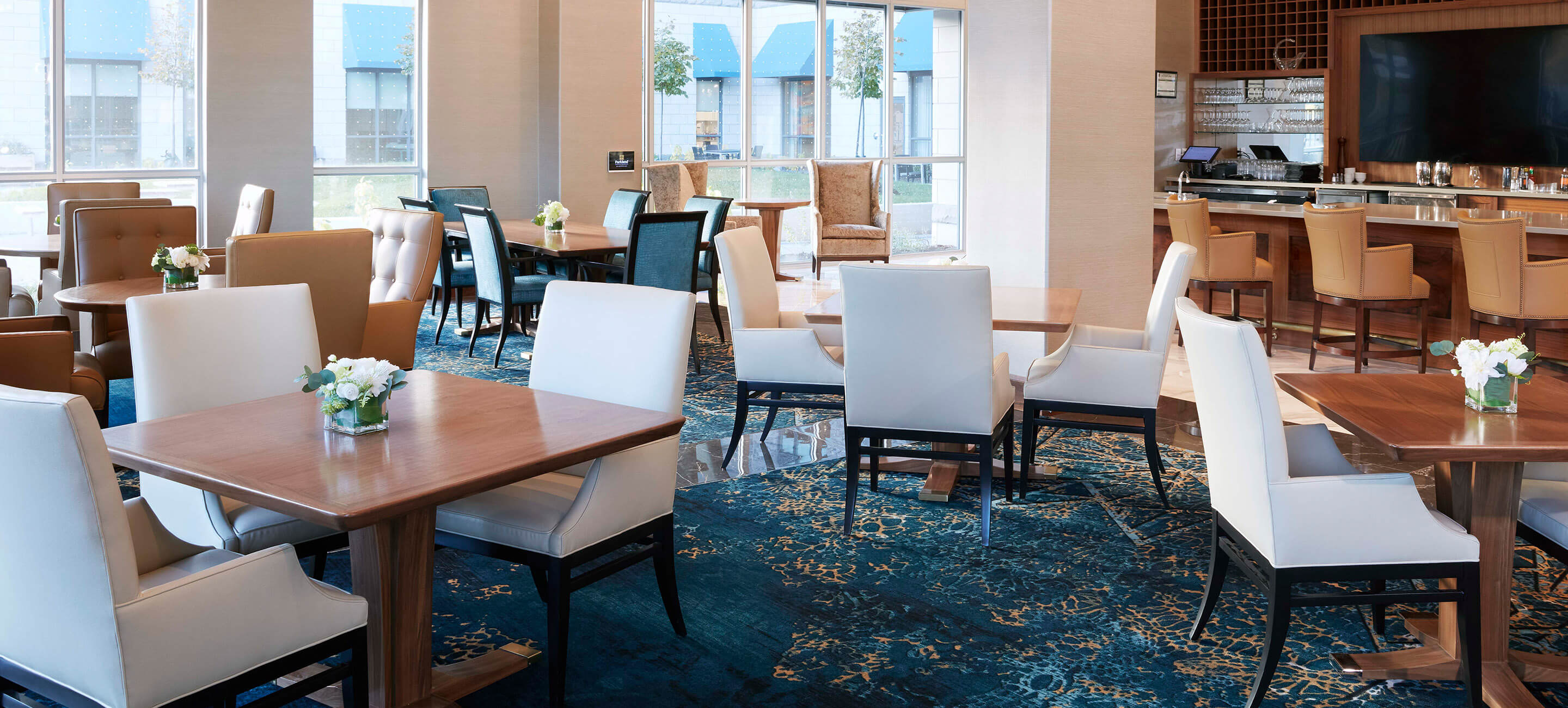 Dining room in Parkland facility with set tables and bar in background, high ceilings with large windows, and carpeted floors