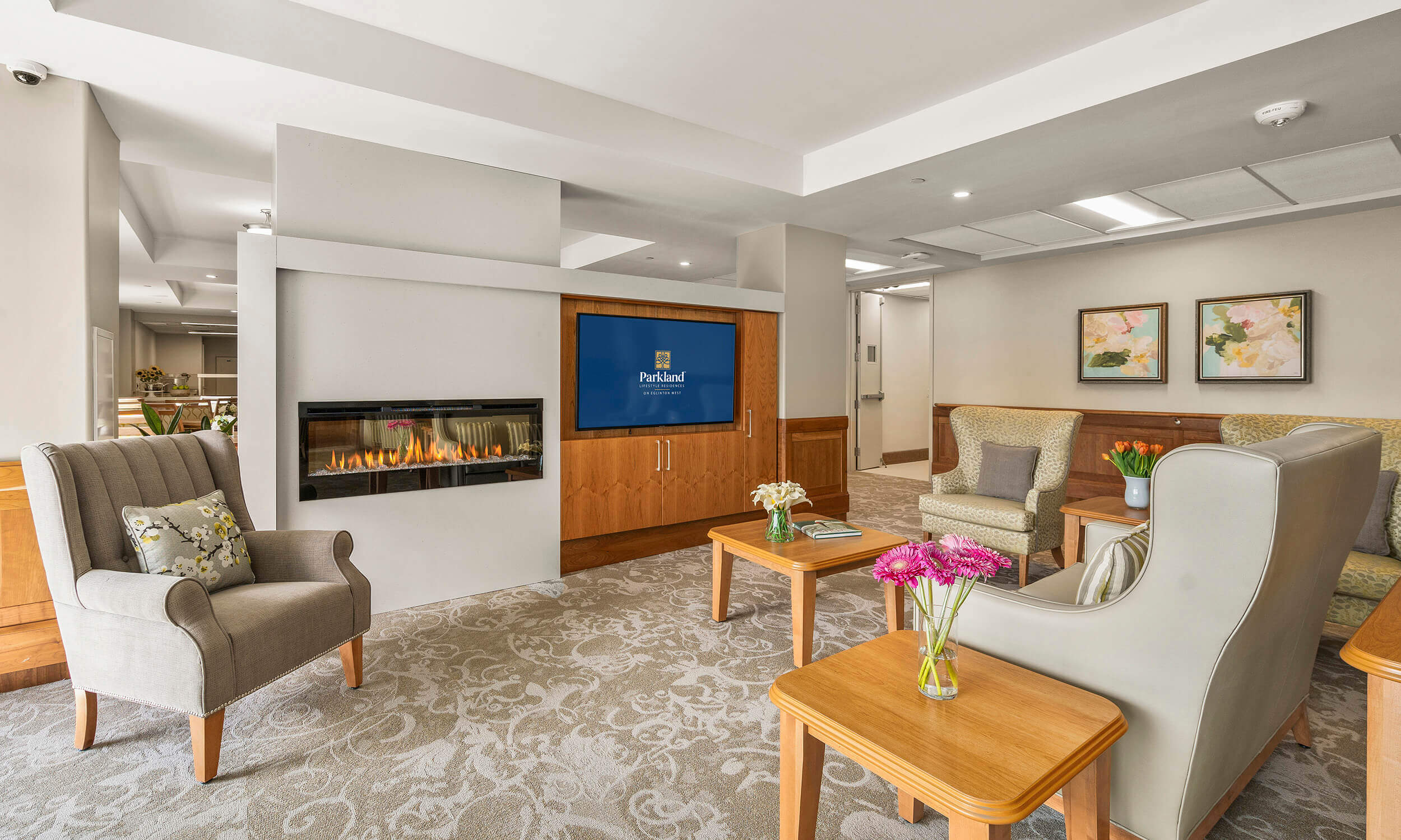 Lobby of Parkland Residence with beige and wooden furniture surrounding TV that displays Parkland logo