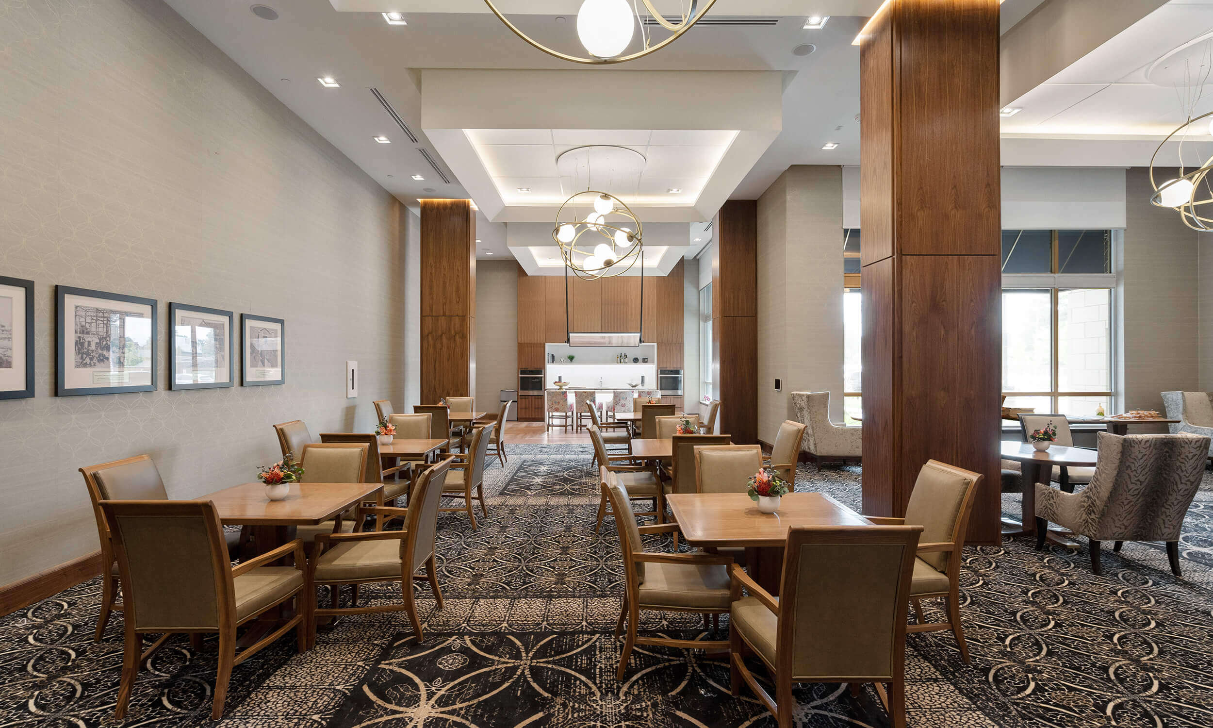 Dining room in Parkland facility with set tables and shared kitchen in background, high ceilings with large windows, and carpeted floors