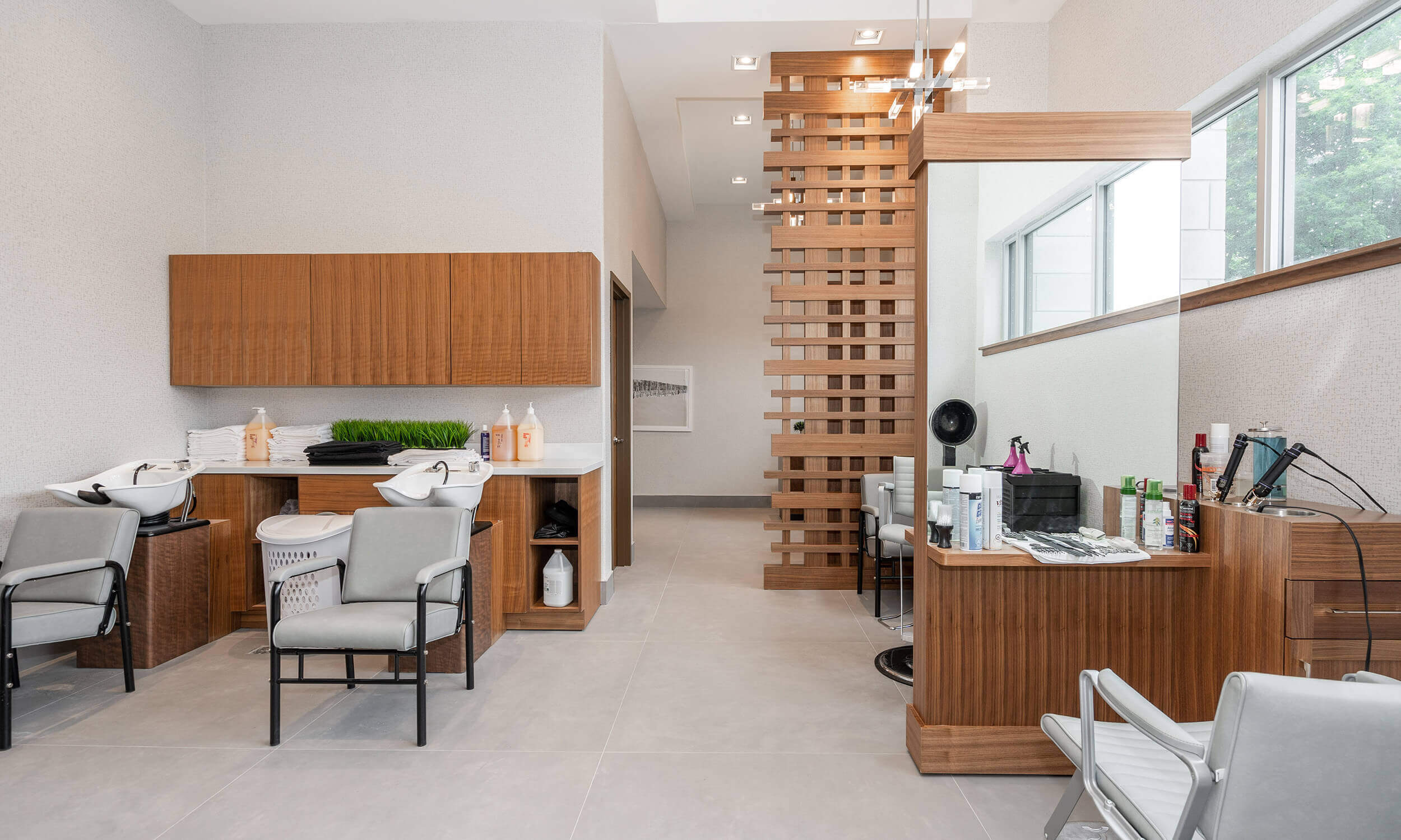 Salon in Parkland Facility with two hair washing stations in front of wooden storage cabinets on one side, and hair styling stations with chair and mirror on the other side