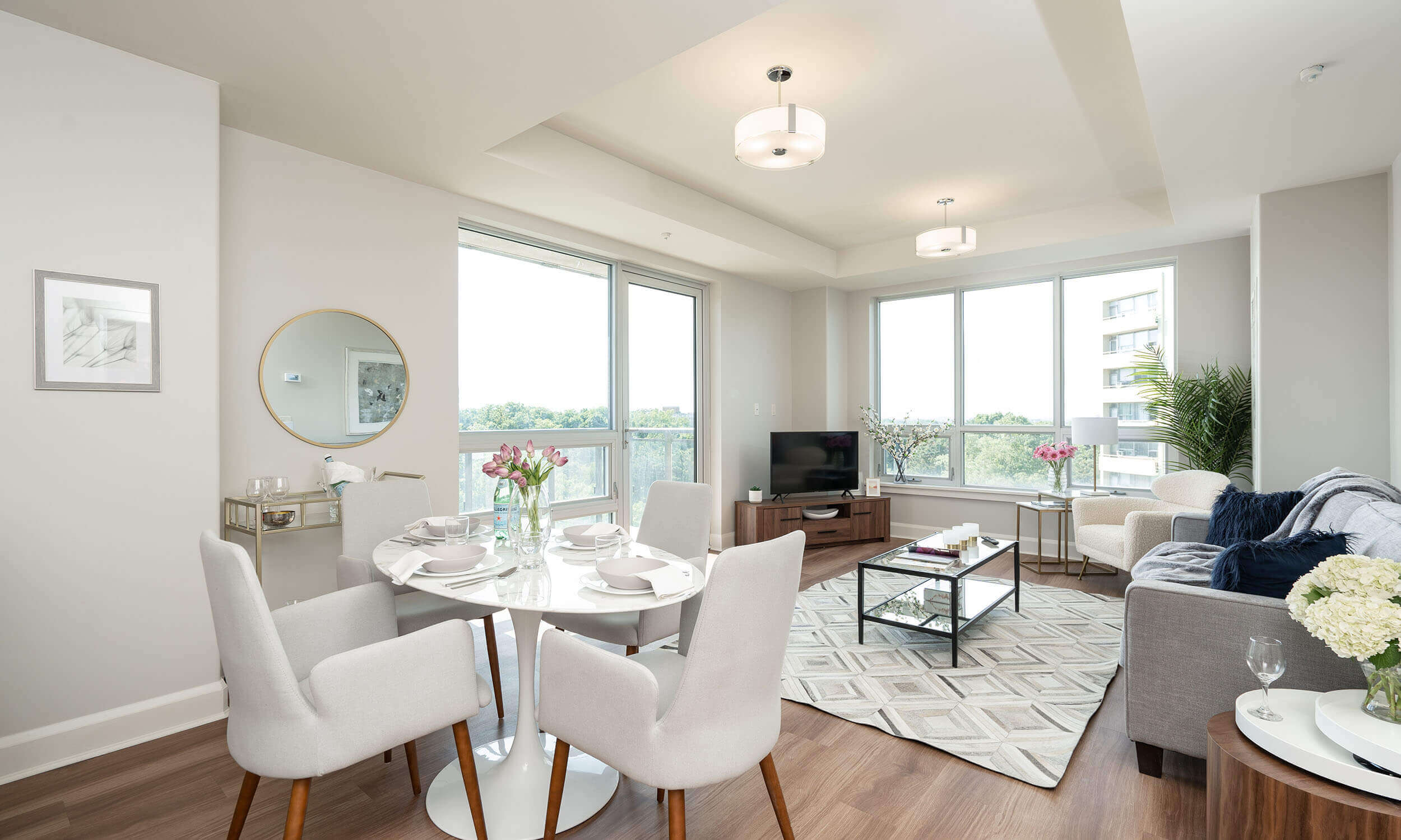 Suite in retirement home with white dining table and shares and living room with television and grey couch