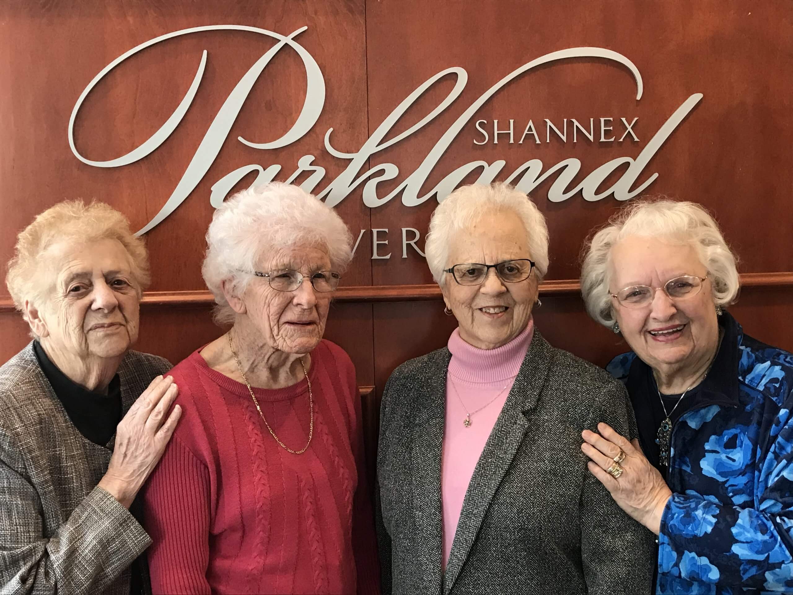 Four senior women smiling in front of Shannex Parkland sign