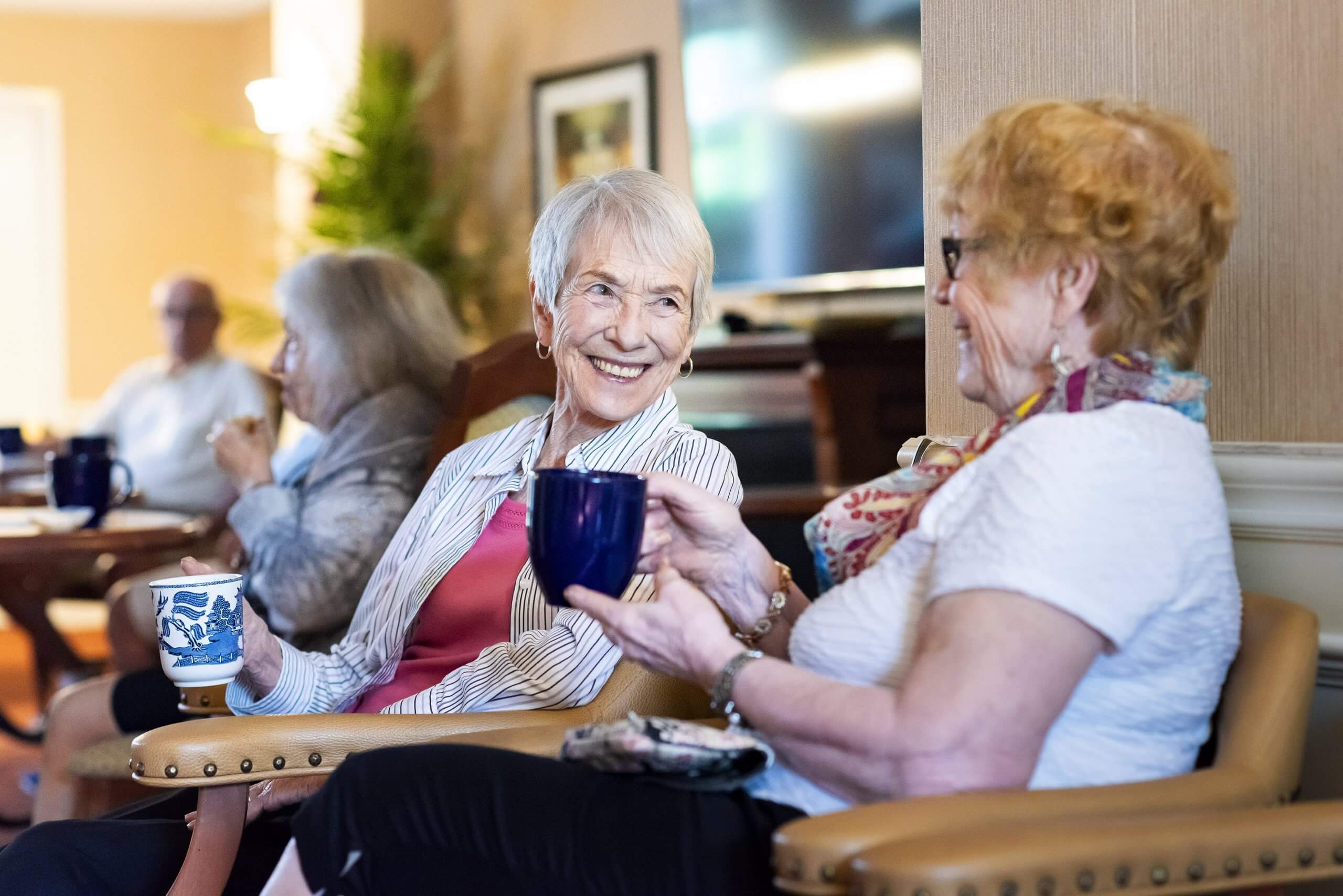 Two senior women drinking coffee and smiling at each other